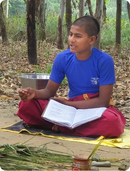 Student seated on a mat reciting from an open scripture