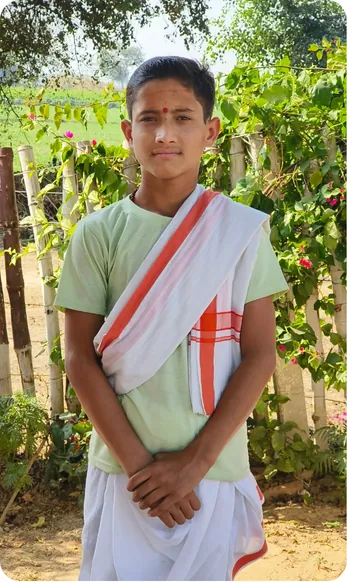 Gurukul student standing with folded hands beside a bamboo fence