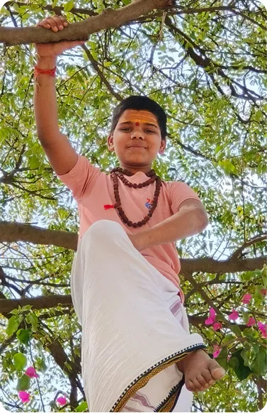 Student climbing a tree branch in the gurukul grounds